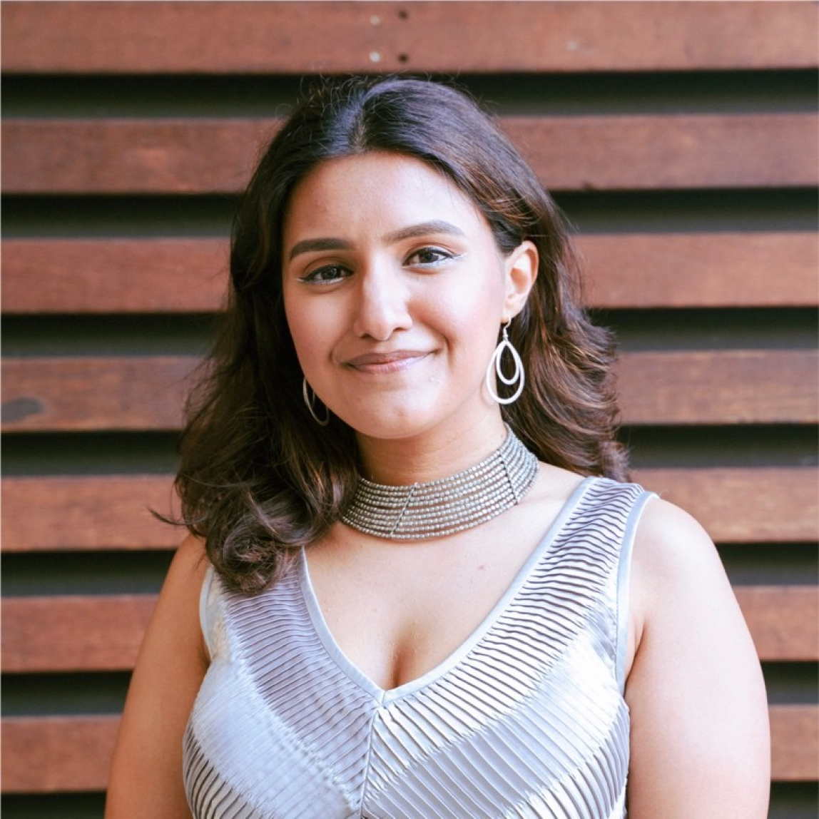 Photo of woman with white dress, black hair in front of horizontal dark wooden beam wall.